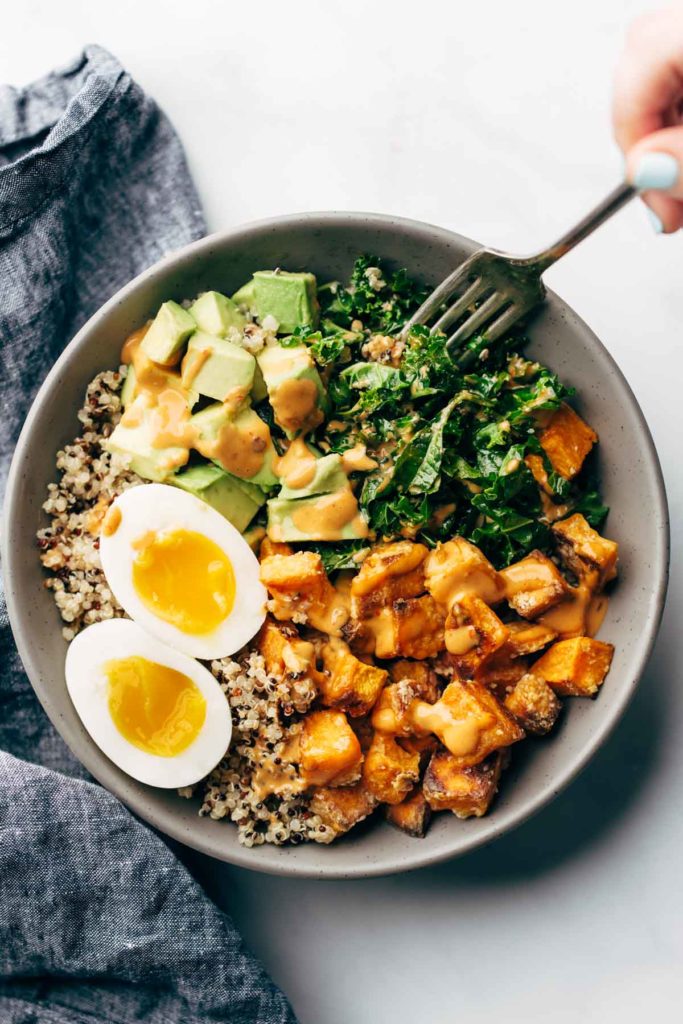 A loaded bowl with rice, eggs, greens, and other ingredients photographed from overhead