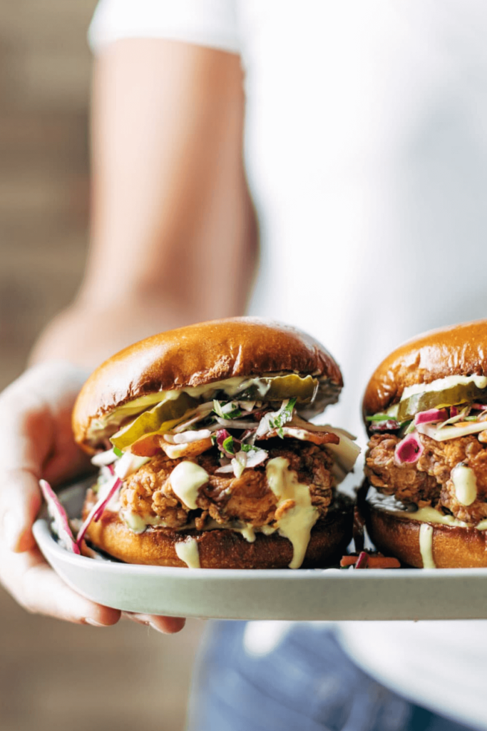 A woman holding a plate with two loaded burgers