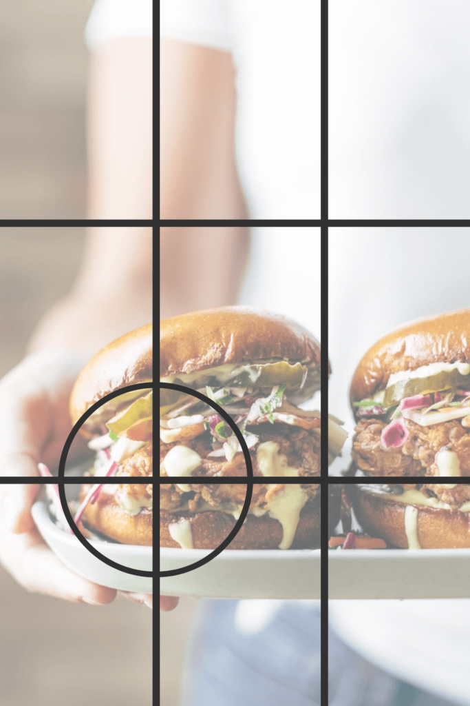 A woman holding a plate with two loaded burgers with lines drawn on to indicate the rule of thirds