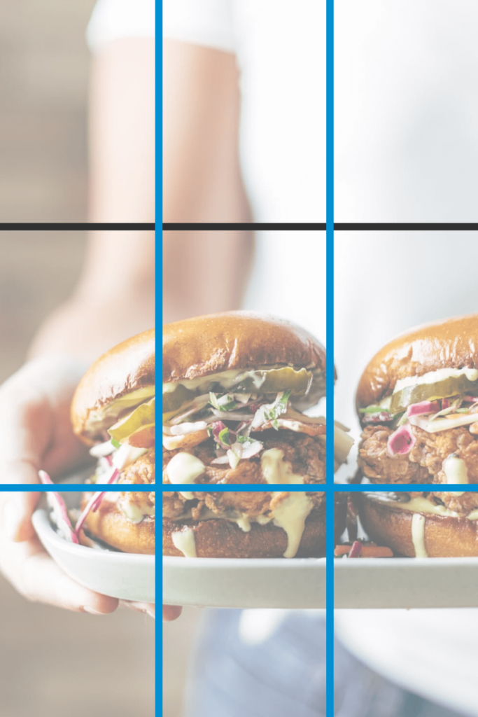 A woman holding a plate with two loaded burgers with black and blue lines drawn on to indicate the rule of thirds