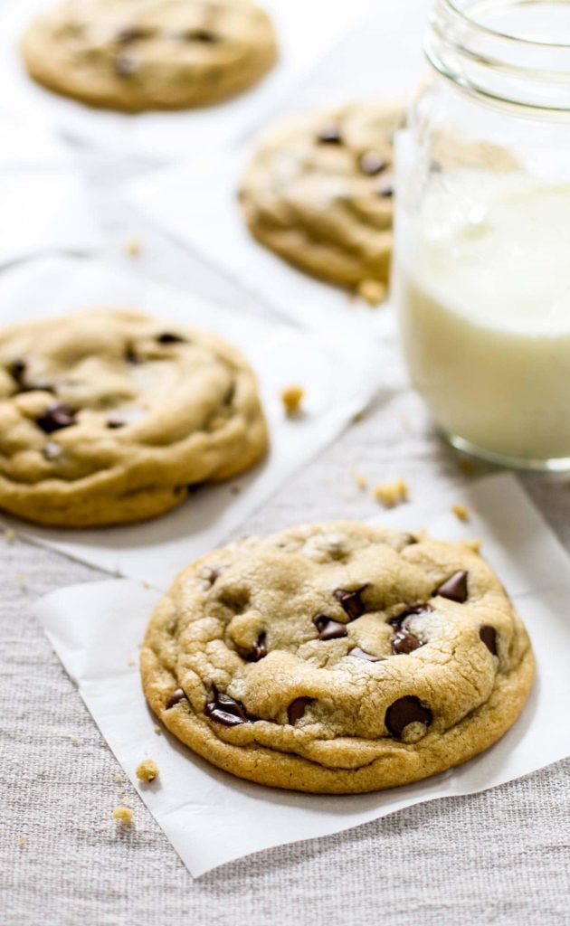 Chocolate chip cookies on parchment paper and a glass of milk shot at three-fourths height