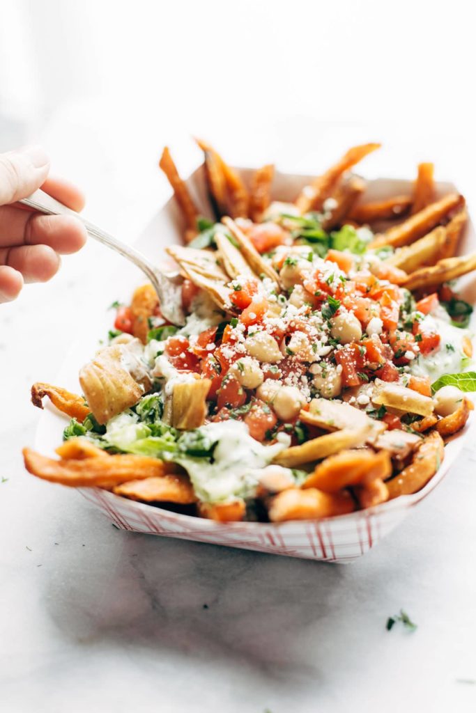 A container of loaded fries and a hand reaching in with a fork shot at three-fourths height