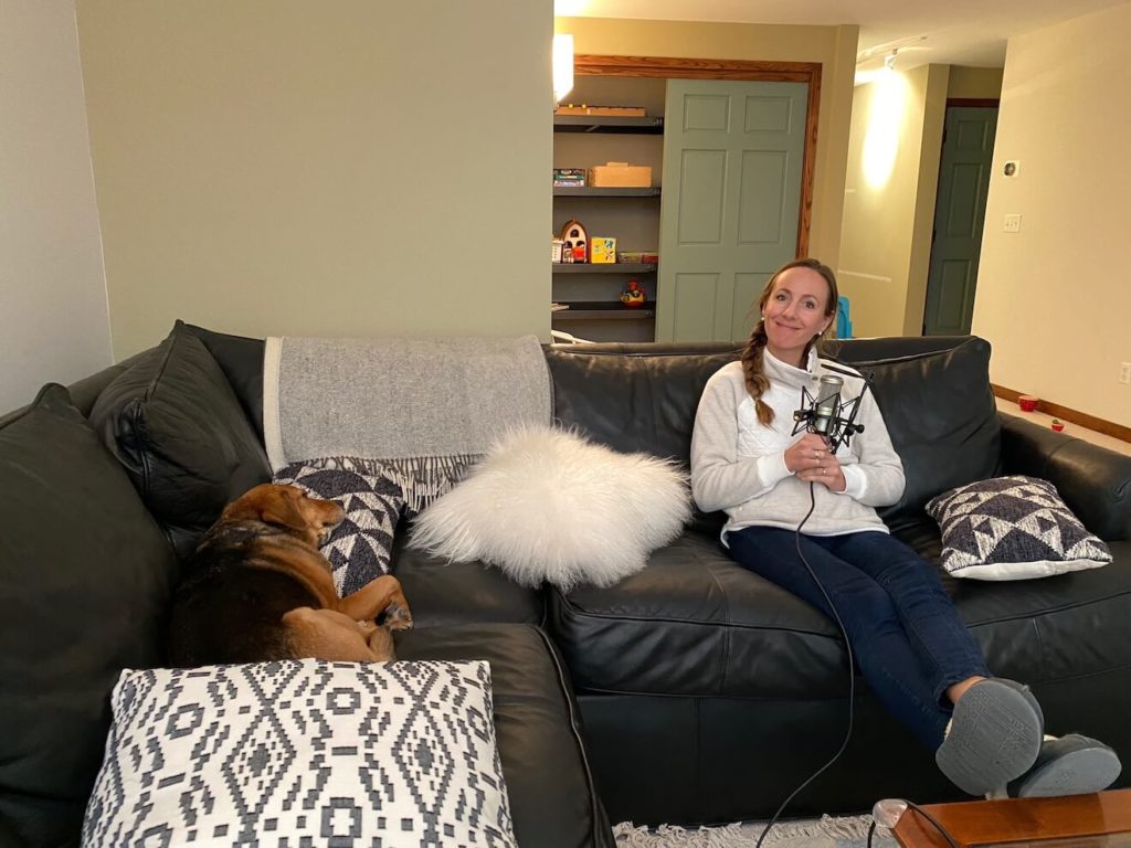 a picture of Lindsay Ostrom with a microphone on a couch with Sage the dog