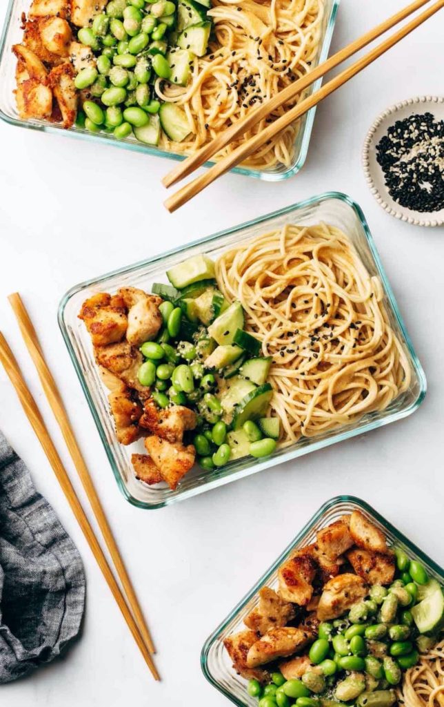 Overhead shot of sesame noodle bowls in storage containers with chopsticks next to them
