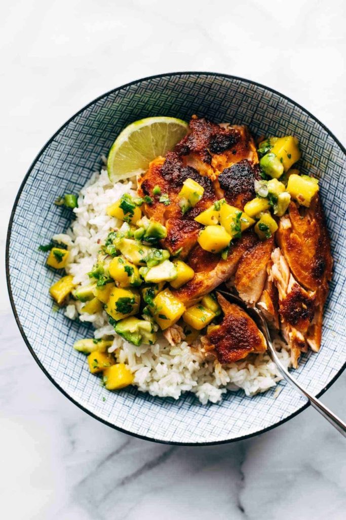 A bowl of BBQ salmon, mango salsa, and a lime over white rice