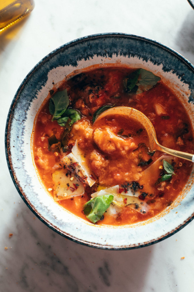 Bowl of tomato soup with basil and a gold spoon