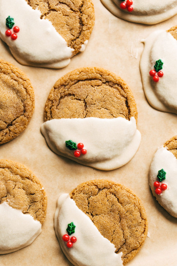 Molasses cookies dipped in white chocolate with holly decoration on parchment paper
