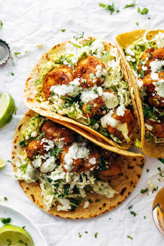 shrimp tacos with coleslaw on a white background with limes and herbs scattered around