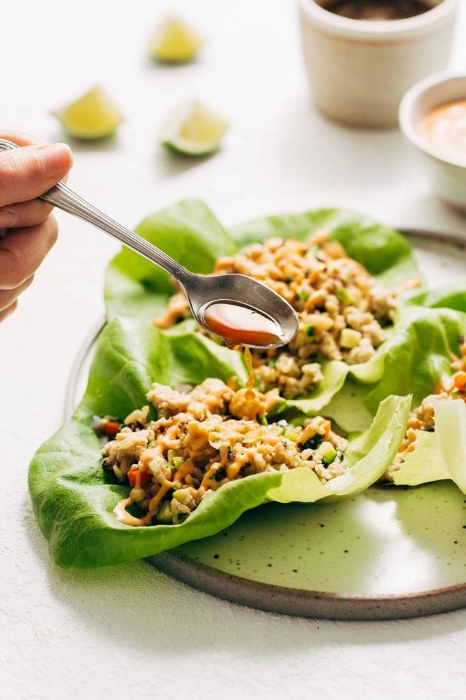 Hand spooning sauce onto a plate of chicken lettuce wraps
