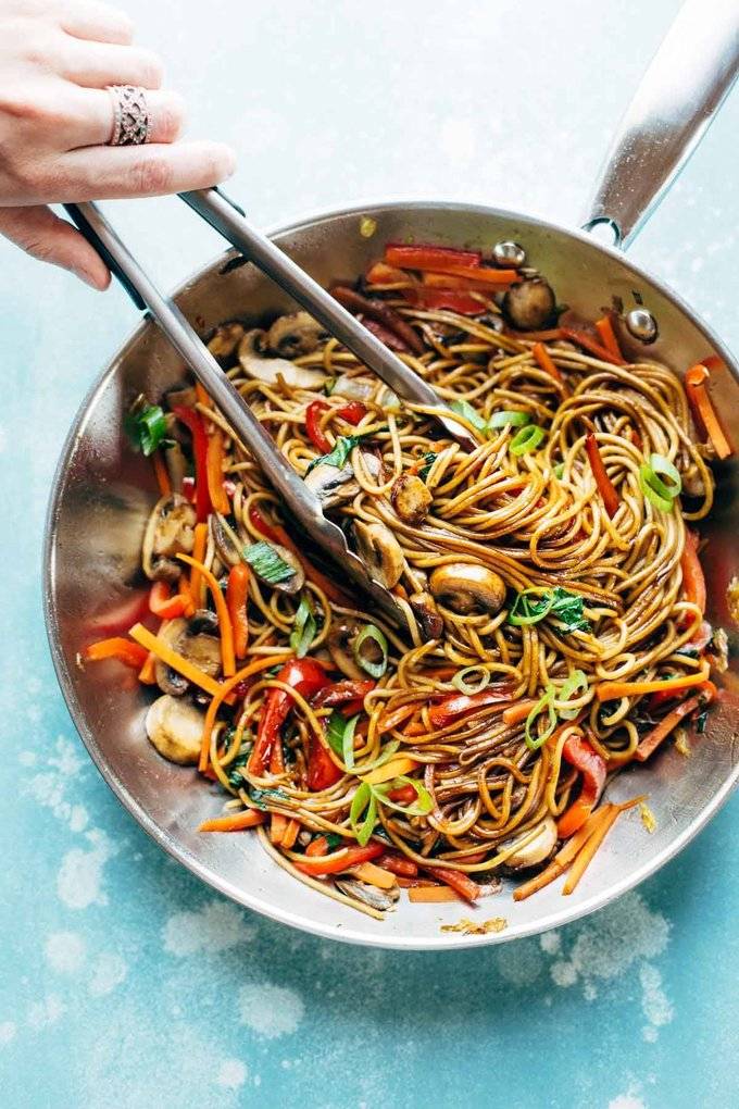 Tongs gripping some lo mein out of a pan