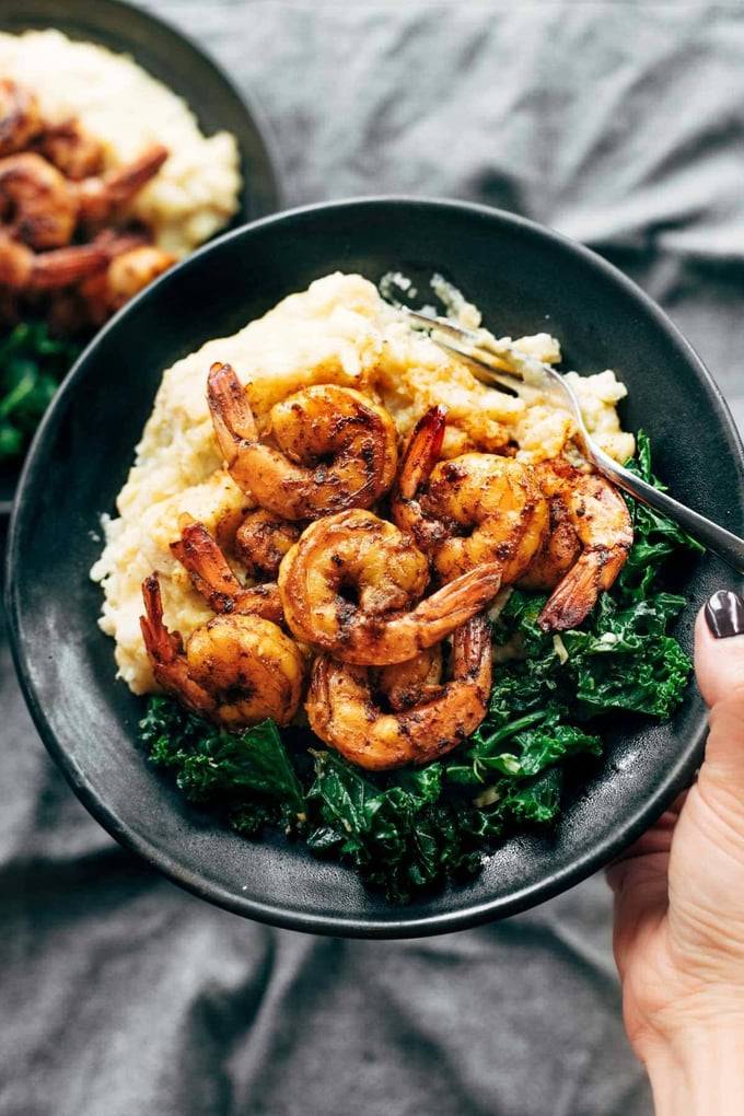 Hand holding a bowl of shrimp, kale, and risotto 