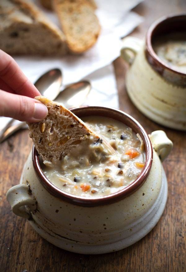 Two bowls of soup and a person dipping a piece of bread into the soup 