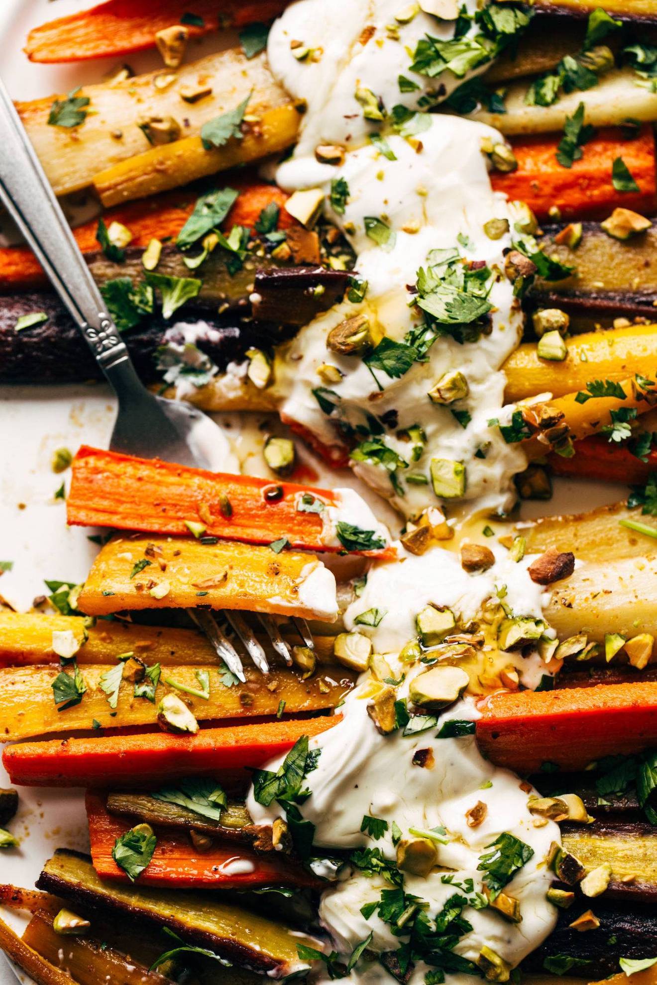 A photograph of roasted carrots with a yogurt sauce, pistachios, and parsley.